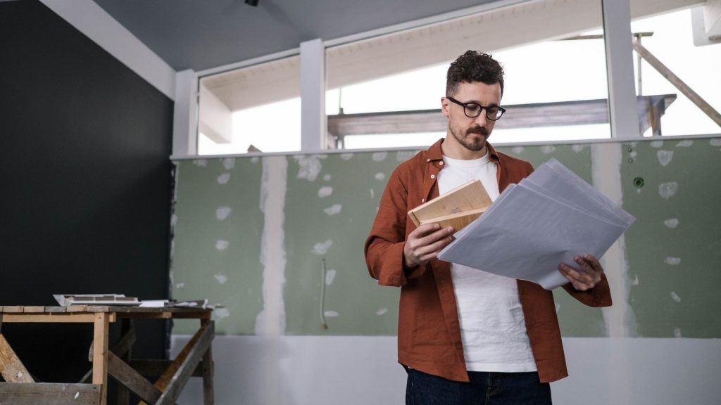 Mann mit Brille studiert Planunterlagen in einem Raum im Umbau