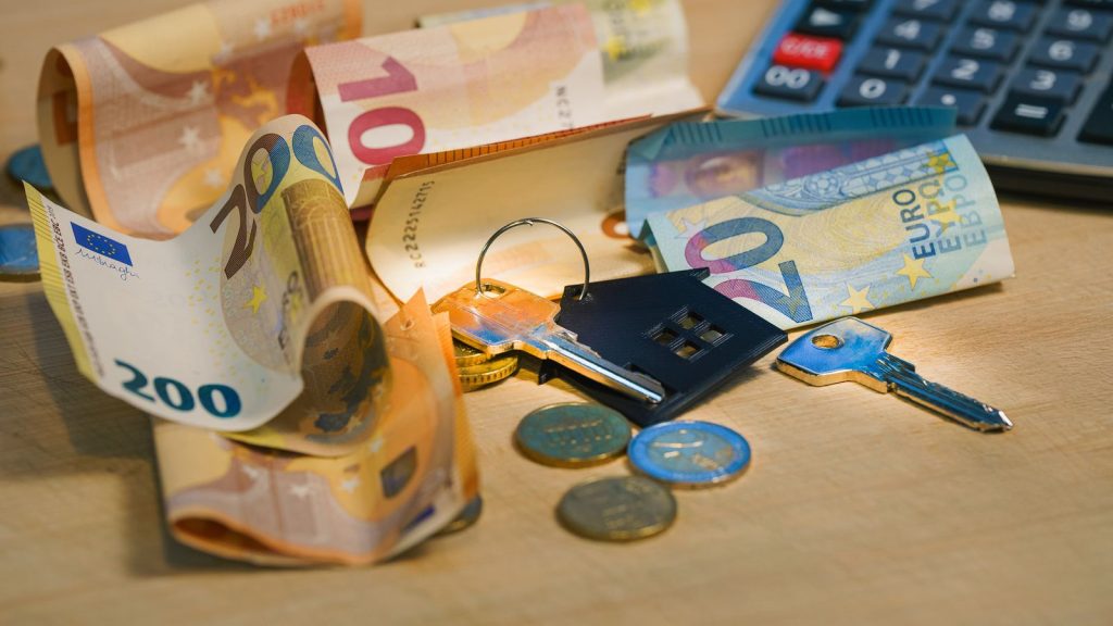 Euro-Scheine, Münzen, Schlüssel mit Haus-Anhänger und Taschenrechner auf einem Holztisch