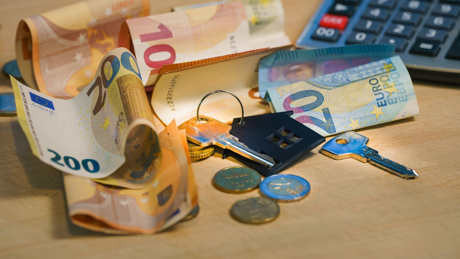 Euro-Scheine, Münzen, Schlüssel mit Haus-Anhänger und Taschenrechner auf einem Holztisch