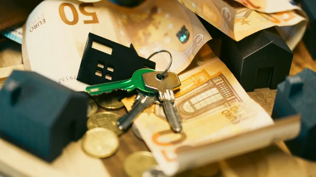 Euro-Scheine, Münzen und Hausschlüssel mit kleinen Hausmodellen